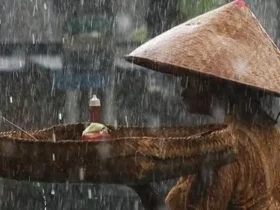 Seorang ibu kehujanan berjalan di bawah langit mendung — simbol ketahanan manusia di tengah krisis iklim.