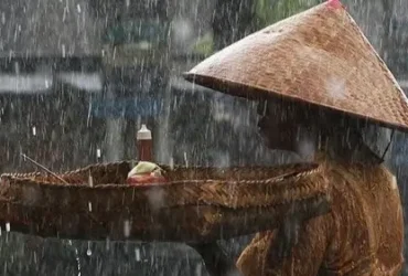 Seorang ibu kehujanan berjalan di bawah langit mendung — simbol ketahanan manusia di tengah krisis iklim.