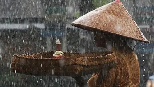 Seorang ibu kehujanan berjalan di bawah langit mendung — simbol ketahanan manusia di tengah krisis iklim.