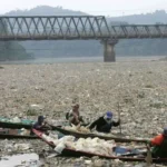 Permukaan sungai berwarna gelap dengan busa — tanda pencemaran sungai akibat pembuangan limbah industri.