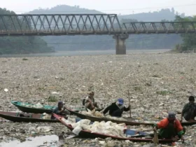 Permukaan sungai berwarna gelap dengan busa — tanda pencemaran sungai akibat pembuangan limbah industri.