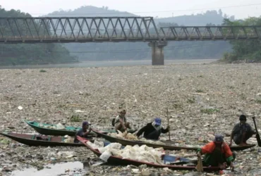 Permukaan sungai berwarna gelap dengan busa — tanda pencemaran sungai akibat pembuangan limbah industri.