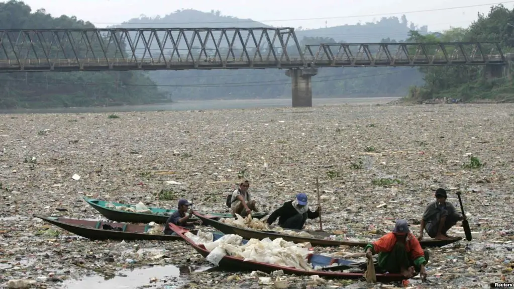 Permukaan sungai berwarna gelap dengan busa — tanda pencemaran sungai akibat pembuangan limbah industri.